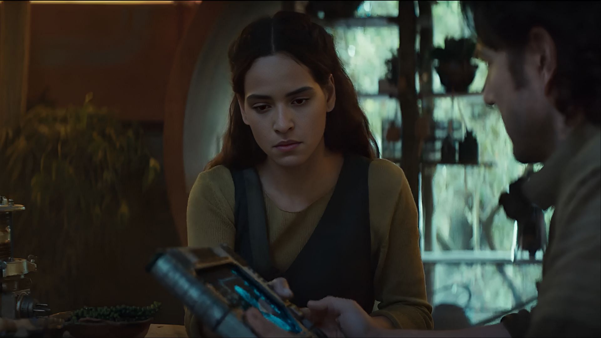 Bix carefully studies the device handed to her, a moment that reflects her cautious trust and growing involvement in the rebellion. (Image via Disney+)